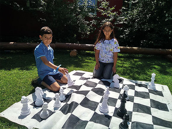 Zwei Kinder auf einer Schachbrett-Matte | Die Fondsdepot Bank unterstützt die Christian-Wolfrum-Grundschule beim Ausbau des Pausenhofbereichs